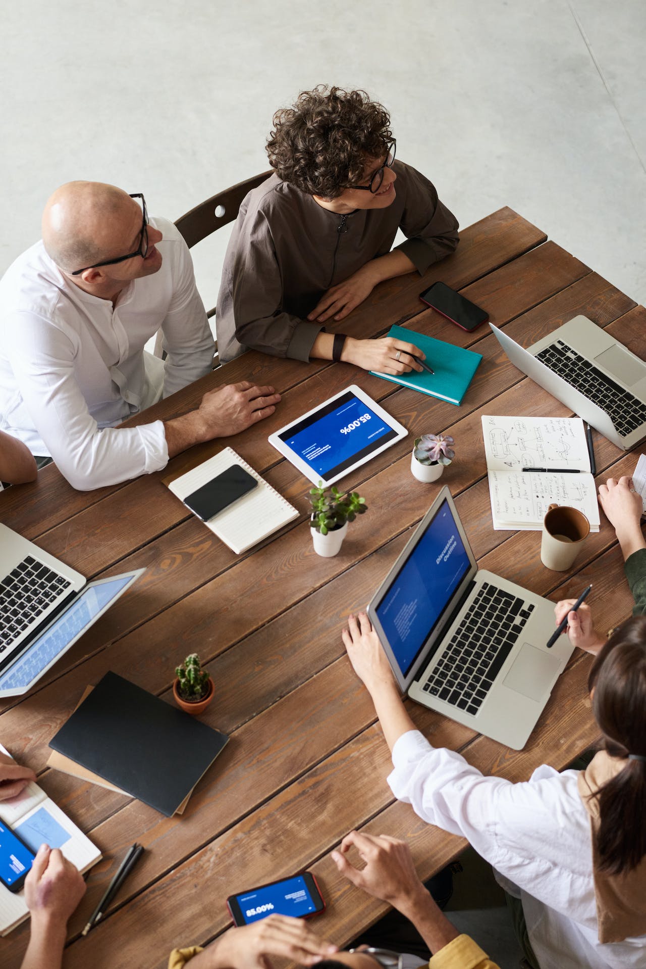 Grupa ludzi siedzących na spotkaniu biznesowym, mająca na stole laptopy i notesy